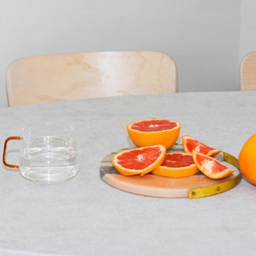 A calm table setting with a glass and a plate of fresh sliced blood oranges on a marble board